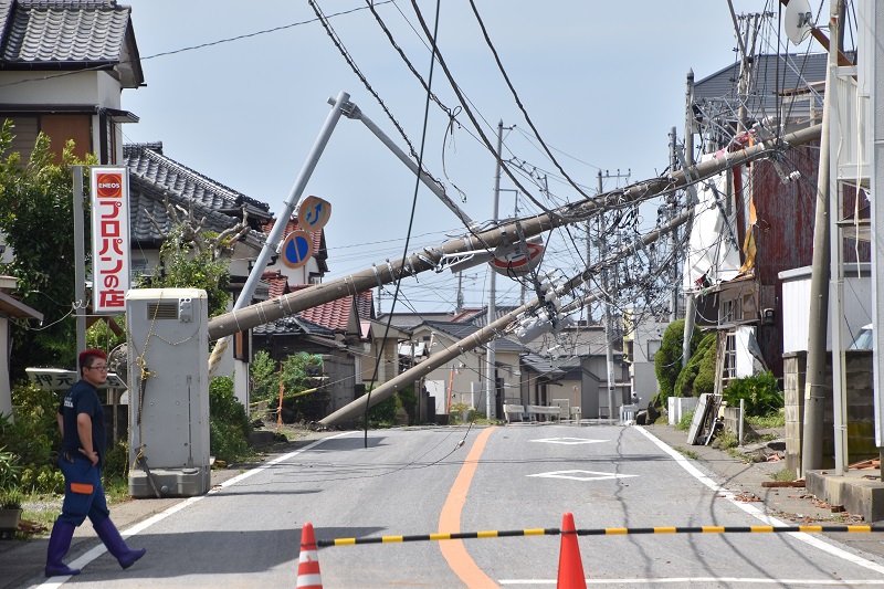 連なるようにして反対側の民家に倒れ込む電柱＝９月９日午前１１時半ごろ、館山市船形
