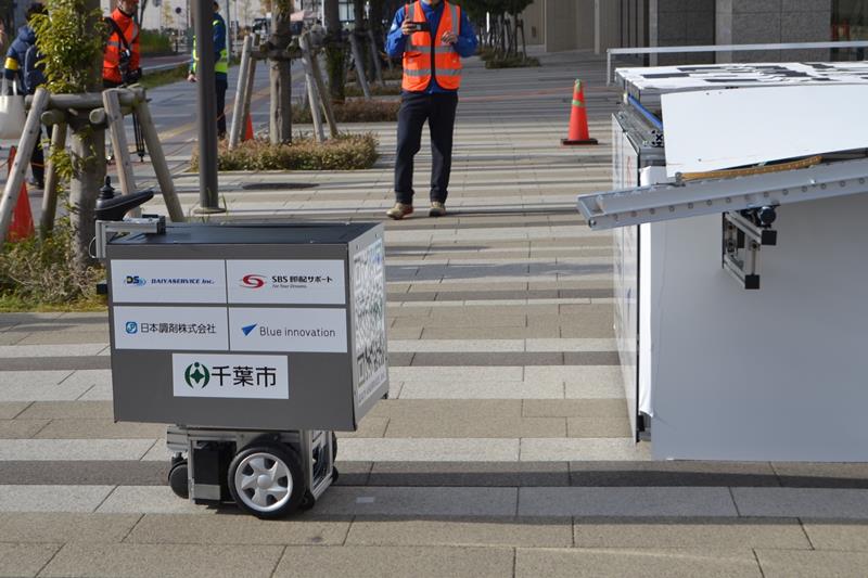 ドローンポート(右)から荷物を自動で受け取り、マンション内へ走行していく地上配送ロボット=20日、千葉市美浜区