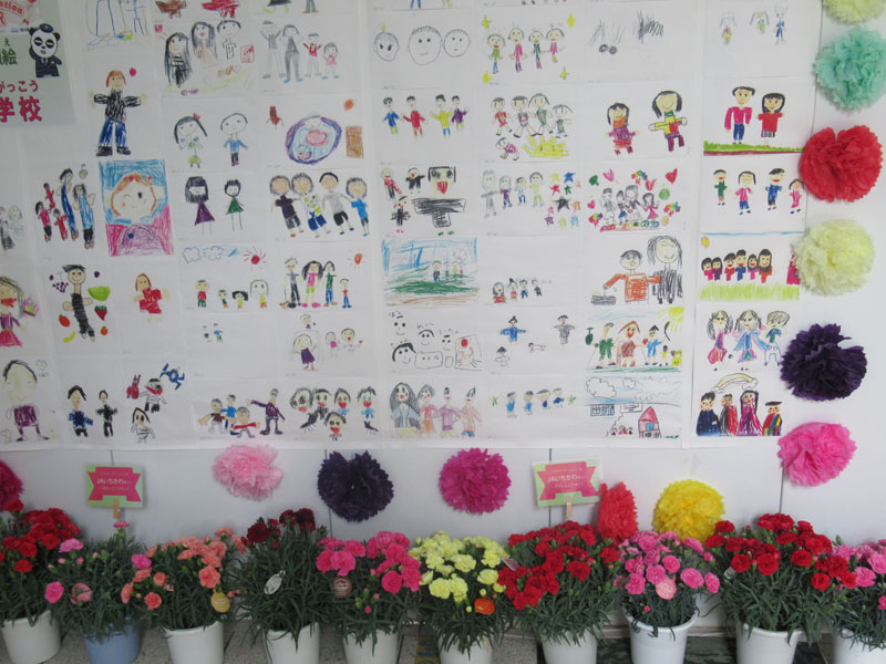 駅改札前に飾られた、近くの小学校などの子どもたちが描いた家族の絵。下はJAいちかわ寄贈のカーネーション=30日、市川市