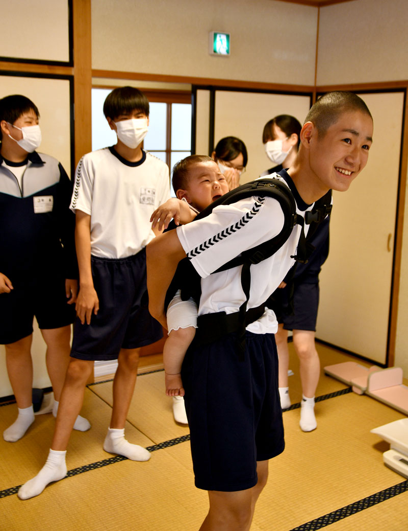 体験授業でおんぶに挑戦する生徒＝東庄町立東庄中学校
