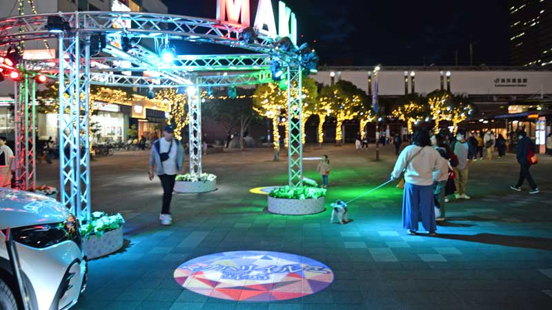 「マクハリイルミ」のイベントに初登場したオブジェ「レインボーサークル」。樹木を装飾した光るオーナメントなどイルミネーションを楽しむ市民ら＝９日、ＪＲ海浜幕張駅前