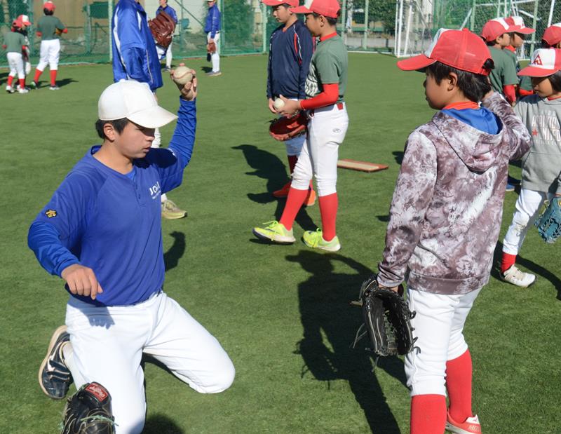 少年野球チームの児童（手前右）にボールの投げ方を教える城西国際大の選手＝東金市