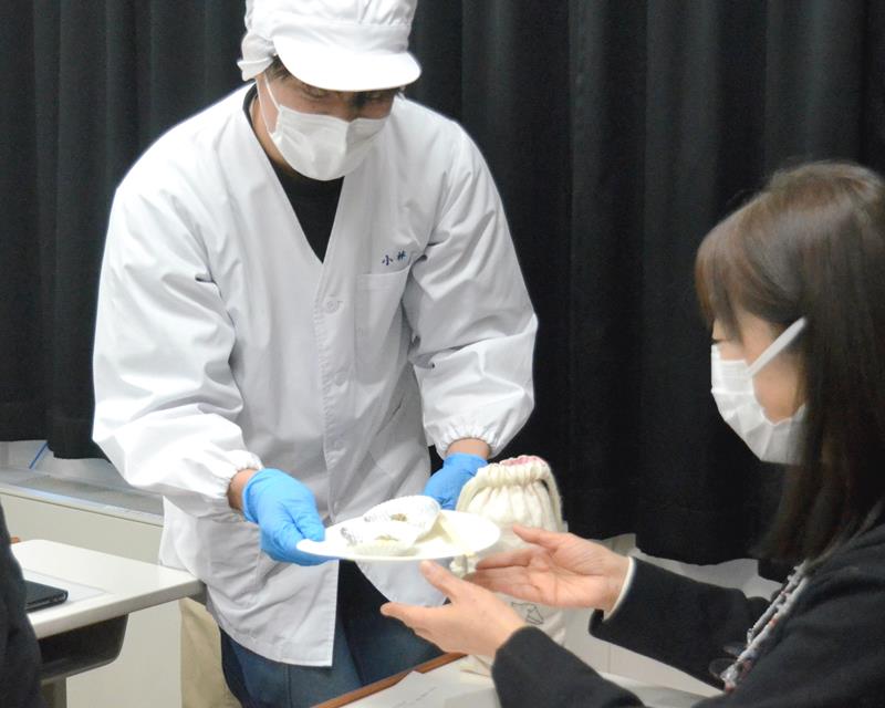 加工食品製造のプロジェクト発表会で、実際に作った食品を参加者に配る県立農業大学校の学生（左）＝東金市