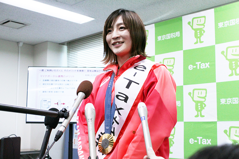 スマホを使った確定申告を模擬体験後、報道各社のインタビューに答える角田選手。首にかけているのはパリ五輪の金メダル=30日、千葉市花見川区の千葉西税務署