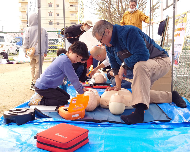 訓練用のＡＥＤを使用し救命の疑似体験をする小学生（左）＝市原市の辰巳台市民広場