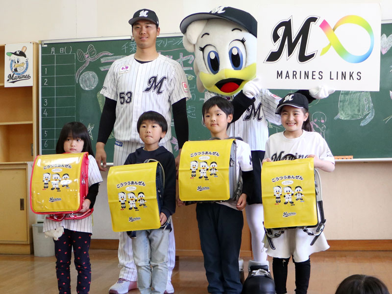 木村投手（後列左）にランドセルカバーを手渡され、うれしそうな新１年生たち＝１６日、千葉市花見川区の市立瑞穂小