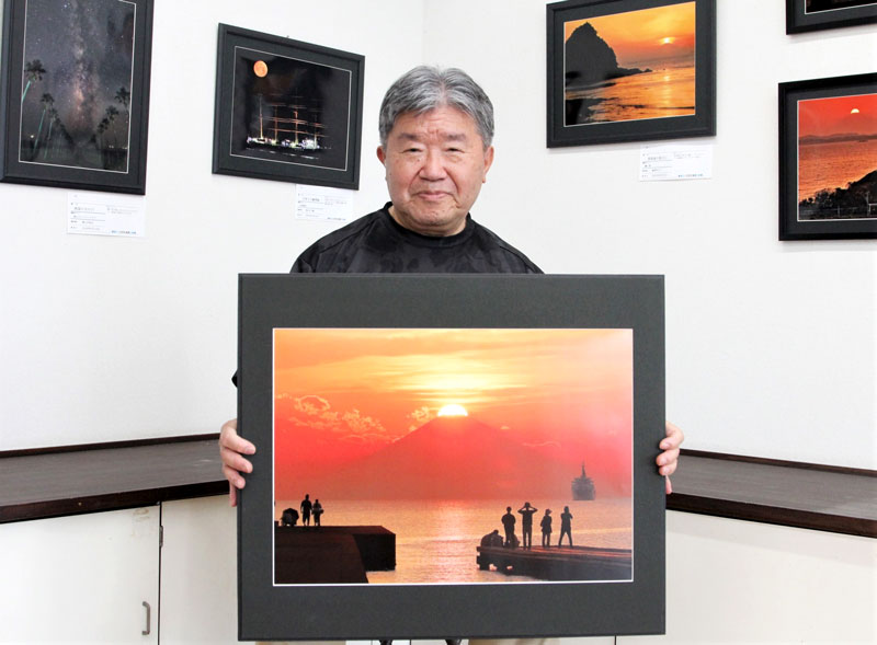 北条海岸で撮影し「夕日百選の鏡ケ浦」と題した作品を見せる小宮さん＝館山市